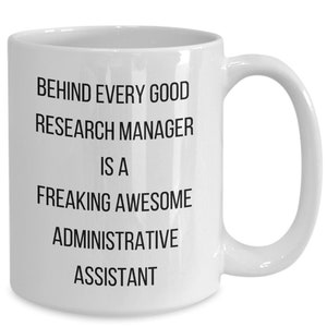May include: White ceramic mug with a curved handle. The mug features black text that reads: "BEHIND EVERY GOOD RESEARCH MANAGER IS A FREAKING AWESOME ADMINISTRATIVE ASSISTANT."