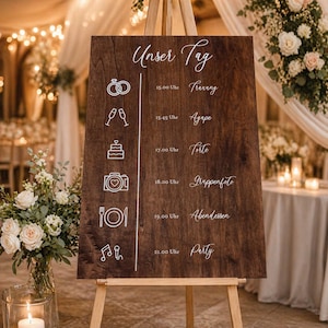 Könnte beinhalten: Ein hölzernes Hochzeitsschild auf einer Staffelei mit den Worten "Unser Tag" oben. Das Schild zeigt einen Zeitplan mit Zeiten und Ereignissen wie "Torte" und "Party" in weißer Schrift. Der Hintergrund umfasst Blumen und sanfte Beleuchtung.