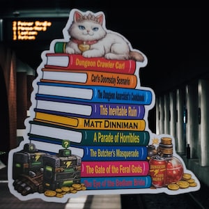 May include: A sticker featuring a white cat wearing a crown atop a stack of books titled Dungeon Crawler Carl, Carl's Doomsday Scenario, The Dungeon Anarchist's Cookbook, This Inevitable Ruin, Matt Dinniman, A Parade of Horribles, The Butcher's Masquerade, The Gate of the Feral Gods, and The Eye of the Bedlam Bride, with game items like a potion and coins.