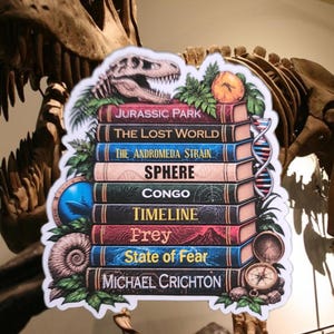 May include: A sticker featuring a stack of books by Michael Crichton, including Jurassic Park, The Lost World, The Andromeda Strain, Sphere, Congo, Timeline, Prey, and State of Fear, decorated with a dinosaur skull, DNA helix, and compass.