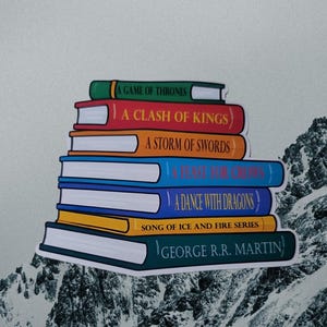 May include: A stack of books from the "Song of Ice and Fire" series by George R.R. Martin. The books have colorful spines with titles like "A Game of Thrones" and "A Clash of Kings". The background features a mountain range.
