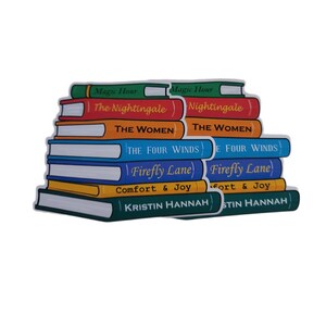 May include: A stack of colorful book-shaped stickers. The titles include "Magic Hour", "The Nightingale", "The Women", "The Four Winds", "Firefly Lane", "Comfort & Joy", and "Kristin Hannah". The stickers are in various colors, including green, red, orange, blue, yellow, and dark green.