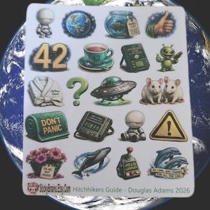 Peut inclure: Une planche d'autocollants illustrant l'univers du Guide du voyageur galactique, comprenant un peignoir blanc marqué Arthur Dent, une serviette verte avec le texte DON'T PANIC, une baleine, des dauphins avec le texte SO LONG, AND THANKS FOR ALL THE FISH et le nombre 42.
