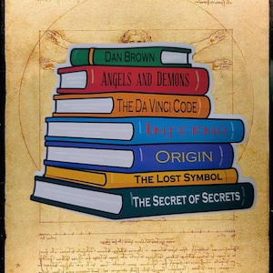 Könnte beinhalten: Ein Stapel aus sieben Büchern mit farbigen Buchrücken, die die Titel Dan Brown, Angels and Demons, The Da Vinci Code, Inferno, Origin, The Lost Symbol und The Secret of Secrets tragen, vor einem pergamentartigen Hintergrund mit Skizzen.