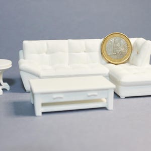 May include: A small white living room set comprising a sectional sofa, coffee table, and side table. A one Euro coin is placed on the sofa for scale. The furniture is made of a solid, opaque material and is set against a grey background.