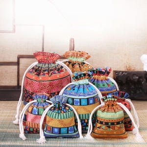 May include: A selection of patterned drawstring bags in various sizes and colours. The bags display geometric and floral designs in shades of red, blue, orange, and green, with white drawstring cords. These decorative bags are suitable for small gifts or storage.