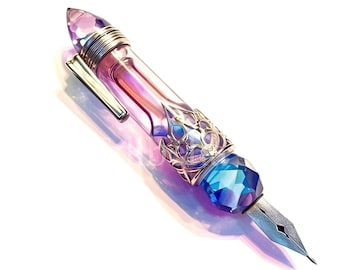 May include: A purple and blue glass fountain pen with a gold-toned metal trim and a decorative crystal-like tip.