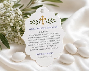 May include: A white scalloped tag with a hole at the top, featuring a gold cross, green leaves, and blue text reading GREEK WEDDING TRADITION, KOUFETA, and the names GEORGE & MARIA with the date AUGUST 23, 2026, surrounded by white candy-coated almonds.