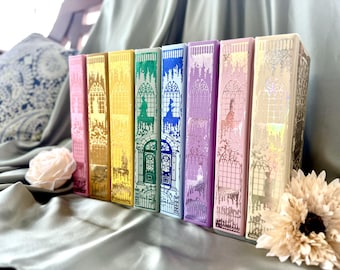 May include: A row of colorful book spines with intricate gold foil designs. The books are in shades of pink, yellow, green, blue, purple, and cream. Each spine features a different illustration of a castle or architectural element.
