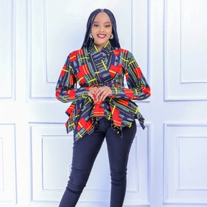 May include: A colorful wrap top with a geometric pattern in red, yellow, and blue. The top has long sleeves and a belted waist. The model is wearing dark blue jeans.
