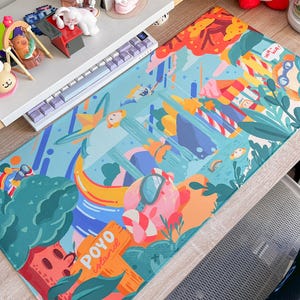 May include: A rectangular desk mat with a colorful, whimsical design featuring cartoon-style illustrations of people, plants, and objects. The mat has a teal background with orange, pink, and green accents. The text "POYO Island" is visible.