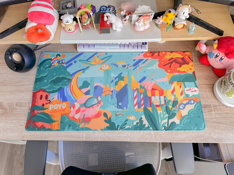 May include: A colorful desk mat featuring a whimsical illustration of a fantasy landscape with cartoonish characters, trees, and buildings. The mat has a blue background with orange, green, and yellow accents. Text on the mat reads "POYO islands" and "WA-WA!"