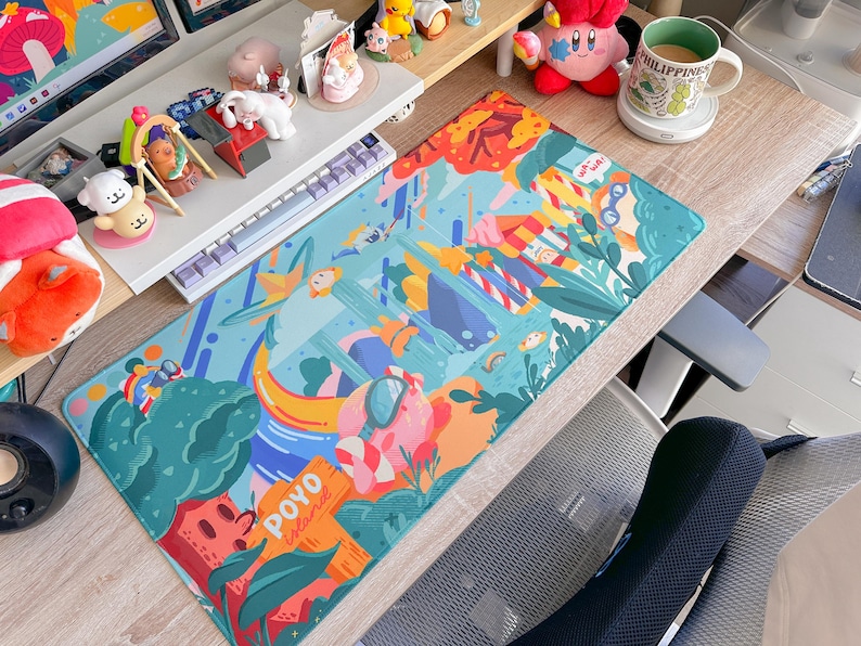 May include: A rectangular desk mat with a colorful, whimsical design featuring cartoon-style illustrations of people, plants, and objects. The mat has a teal background with orange, pink, and green accents. The text "POYO Island" is visible.
