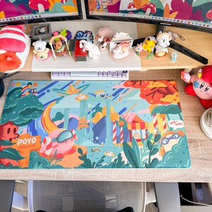 May include: A colorful desk setup featuring a vibrant mousepad with a cartoon landscape design, a keyboard, and various figurines. A plush toy and a mug are also visible. The mousepad has the text "POYO Island".