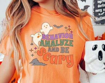 May include: Orange t-shirt with a graphic of ghosts and the text "Behavior Analyze and Be Scary" in a retro font.
