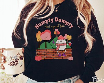 May include: Black sweatshirt with a graphic of a cartoon egg character holding a cup of coffee. The text "Humpty Dumpty Had a Great Fall" is printed on the sweatshirt.