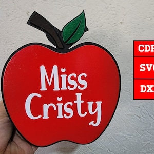 May include: Red apple-shaped sign with a green leaf and the text "Miss Cristy" in white.
