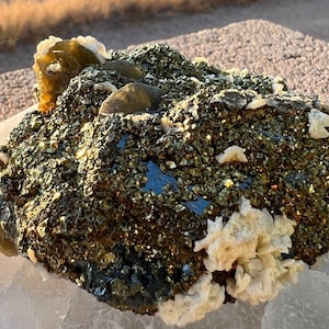 May include: A large, rough, dark brown and gold rock with a cluster of light brown crystals on top. The rock is covered in small, shiny crystals.