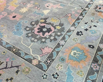May include: A gray rug with a floral pattern in shades of pink, blue, and orange. The rug has a border with a geometric design.