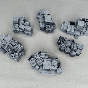 Può includere: Cinque elementi di terreno in miniatura grigi, tra cui casse, botti e altri contenitori di stoccaggio. I pezzi sono disposti in un motivo circolare, adatti per giochi da tavolo o modellismo.