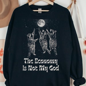 May include: Black sweatshirt with a graphic of three raccoons reaching for a full moon. The text "The Economy Is Not My God" is printed below the graphic.
