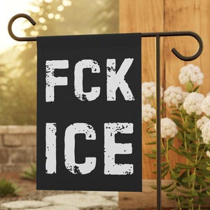 May include: Black garden flag with the white text "FCK ICE". The flag is hanging on a black metal stand in a garden setting. The text has a distressed, textured appearance.