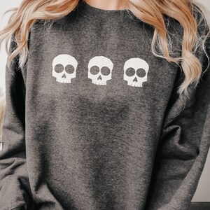 May include: A dark gray sweatshirt with three white skull graphics printed on the front.