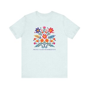 Camiseta "Proteger y defender a los inmigrantes": colorida camiseta de arte popular mexicano con flores. Nadie es ilegal en tierras robadas. Los inmigrantes hacen que Estados Unidos sea grandioso. Heather Ice Blue