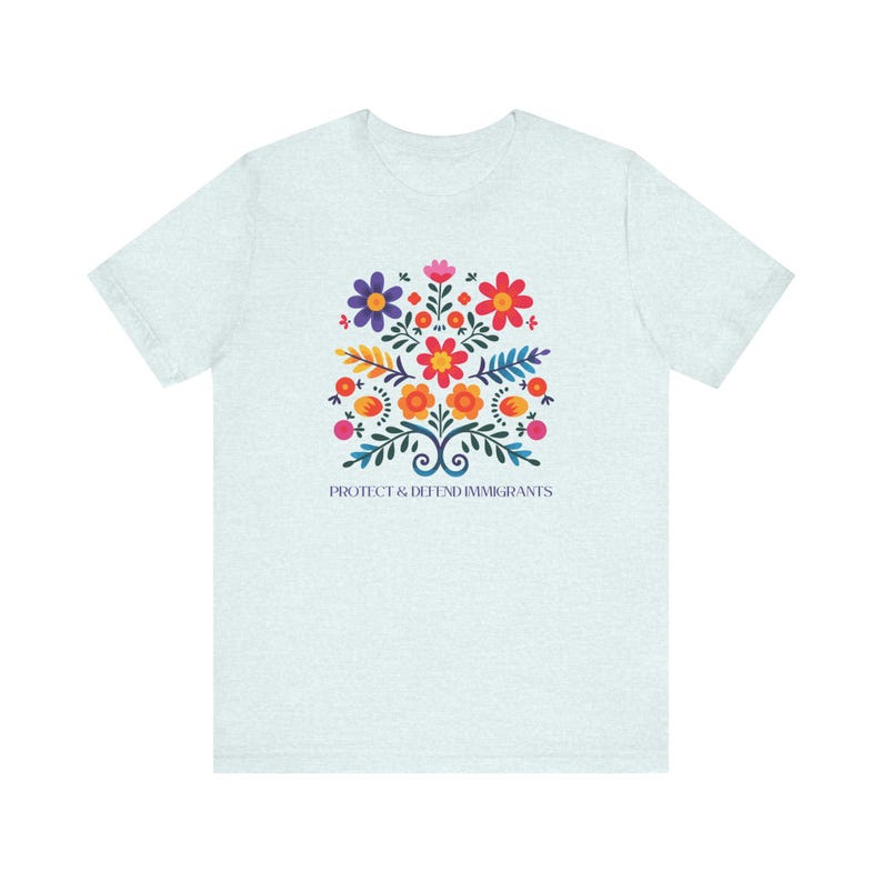 Camiseta "Proteger y defender a los inmigrantes": colorida camiseta de arte popular mexicano con flores. Nadie es ilegal en tierras robadas. Los inmigrantes hacen que Estados Unidos sea grandioso. Heather Ice Blue
