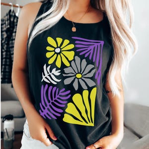 May include: Black tank top featuring a floral design in yellow, gray, white, and purple. The graphic includes stylized flowers and leaves. The top is sleeveless and made of a soft material.