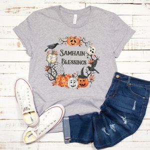 May include: Gray t-shirt with a wreath design featuring pumpkins, crows, and a clock. The wreath has the text "Samhain Blessings" in the center.
