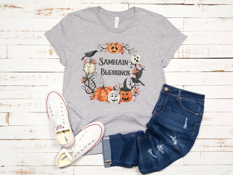 May include: Gray t-shirt with a wreath design featuring pumpkins, crows, and a clock. The wreath has the text "Samhain Blessings" in the center.