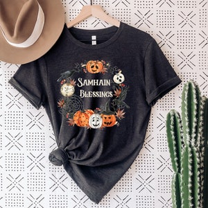 May include: A black t-shirt with a graphic design of pumpkins, crows, and a clock. The text "Samhain Blessings" is printed on the shirt.