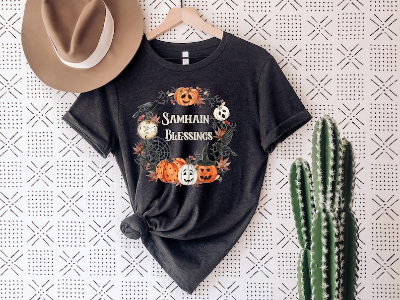 May include: A black t-shirt with a graphic design of pumpkins, crows, and a clock. The text "Samhain Blessings" is printed on the shirt.
