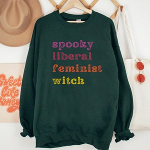 May include: Dark green sweatshirt with the text "spooky liberal feminist witch" in rainbow colors.