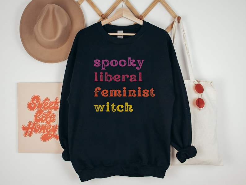 May include: Black sweatshirt with the text "spooky liberal feminist witch" in rainbow colors.