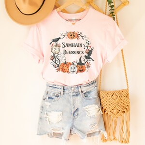 May include: Pink t-shirt with a graphic of a wreath with pumpkins, crows, and the text "Samhain Blessings".