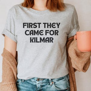 May include: A gray t-shirt with the text "FIRST THEY CAME FOR KILMAR" printed in black.