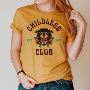 May include: A mustard yellow t-shirt with a black panther head graphic and the text "Childless Cat Lady Club".