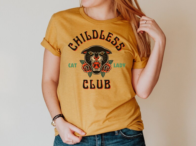 May include: A mustard yellow t-shirt with a black panther head graphic and the text "Childless Cat Lady Club".