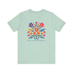 Camiseta "Proteger y defender a los inmigrantes": colorida camiseta de arte popular mexicano con flores. Nadie es ilegal en tierras robadas. Los inmigrantes hacen que Estados Unidos sea grandioso. Heather Prism Mint