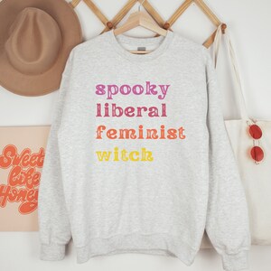 May include: Gray sweatshirt with the text "spooky liberal feminist witch" printed in rainbow colors.