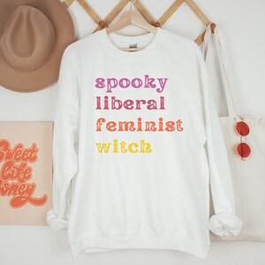 May include: White sweatshirt with the text "spooky liberal feminist witch" in rainbow colors.