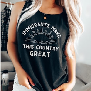 May include: Black tank top with white text that reads "IMMIGRANTS MAKE THIS COUNTRY GREAT". The design includes a sun and waves. The top is worn by a person with blonde hair and a gold necklace.