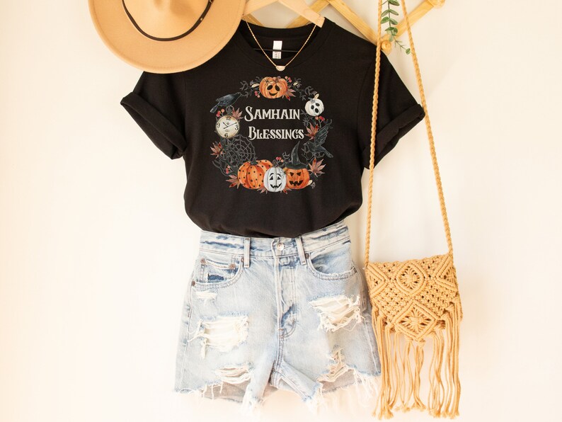 May include: Black t-shirt with a graphic of pumpkins, crows, and a clock with the text "Samhain Blessings".