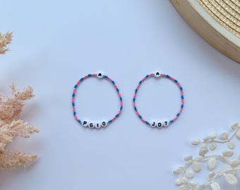 May include: Two beaded bracelets with pink and blue beads. One bracelet spells out the name "PGIO" and the other spells out "JD7".