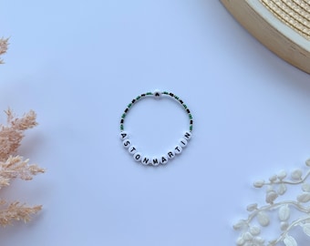 May include: A white beaded bracelet with black lettering spelling out "Aston Martin" and green and black beads.