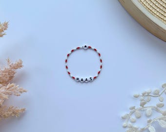 May include: A white and red beaded bracelet with the name "HAAS" spelled out in black letters.
