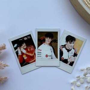 May include: Three polaroid-style photographs of a young man in racing attire. The images show the man in a red racing suit, a white racing suit, and a black and white racing suit. The photos are arranged on a white surface.