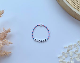 May include: A pink and blue beaded bracelet with the word "ALPINE" spelled out in white beads.